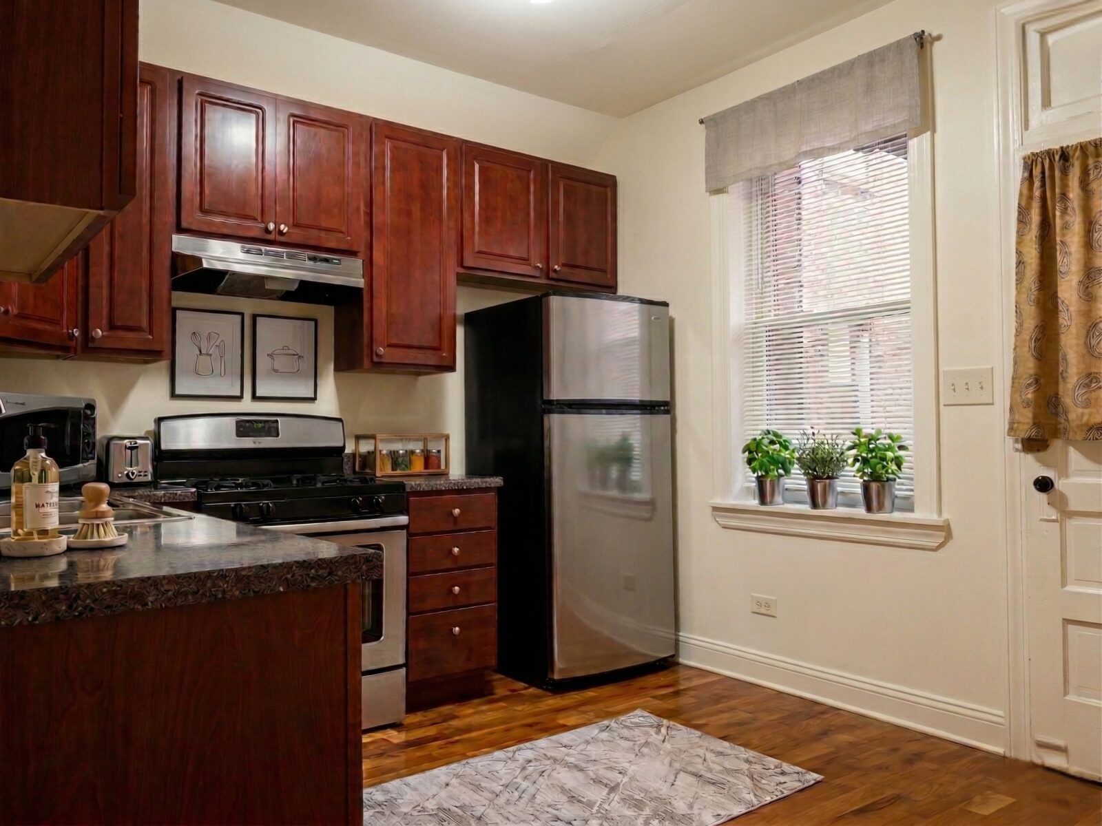 Kitchen with cherry wood cabinets, stainless steel appliances, and small potted herbs on the wind...
