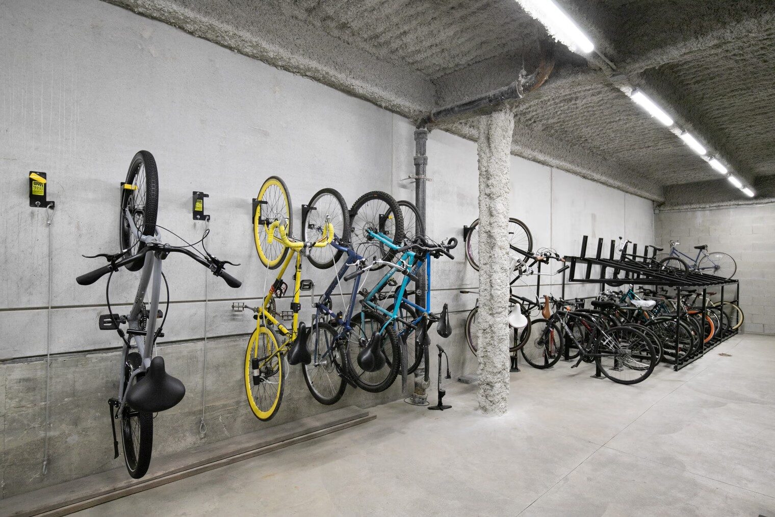 Indoor bicycle storage area with wall-mounted and freestanding bike racks and concrete surfaces.