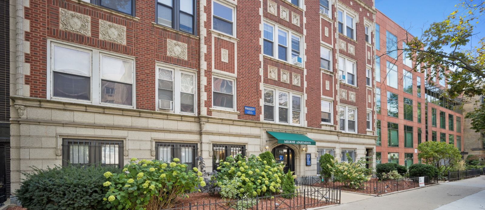 Building exterior showing the red brick facade, ground floor landscaping, and the Melrose Apartme...