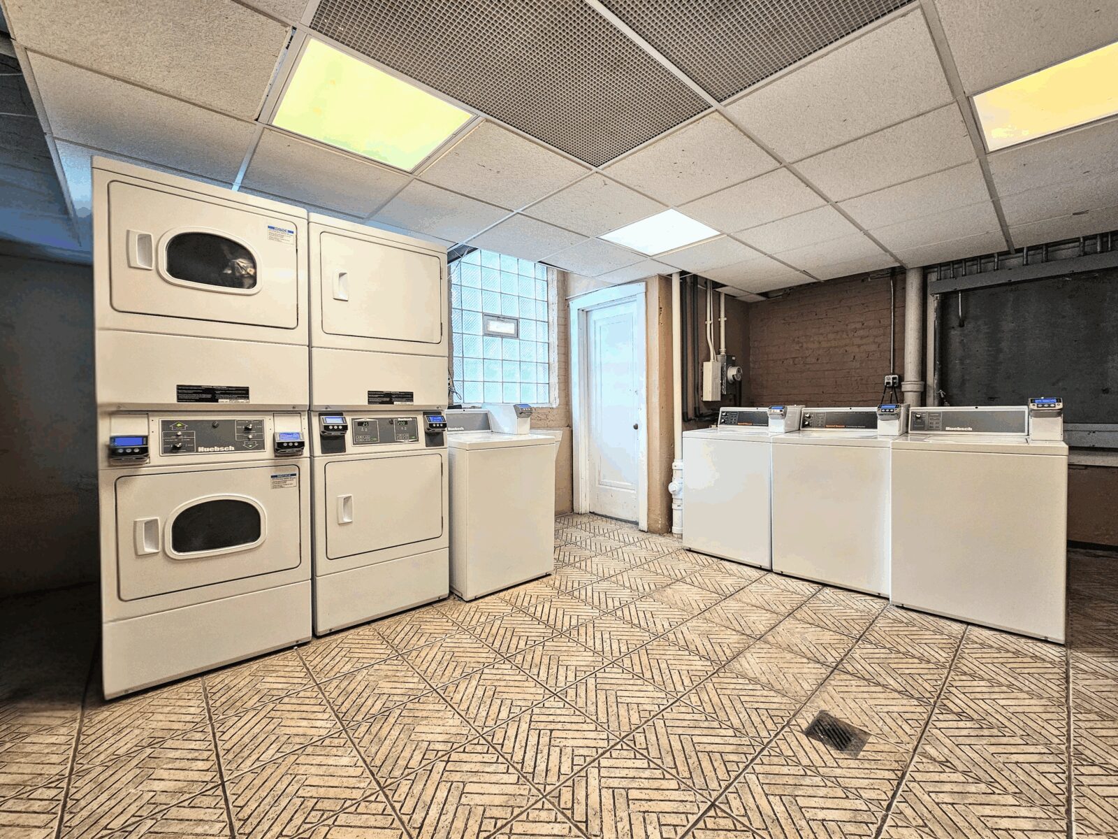 Laundry room with tan patterned tile floor and rows of white stacked washers and dryers.